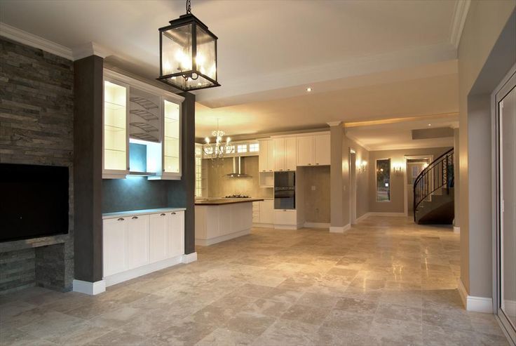 Spacious beige living room with stone fireplace, pendant light, and open kitchen view