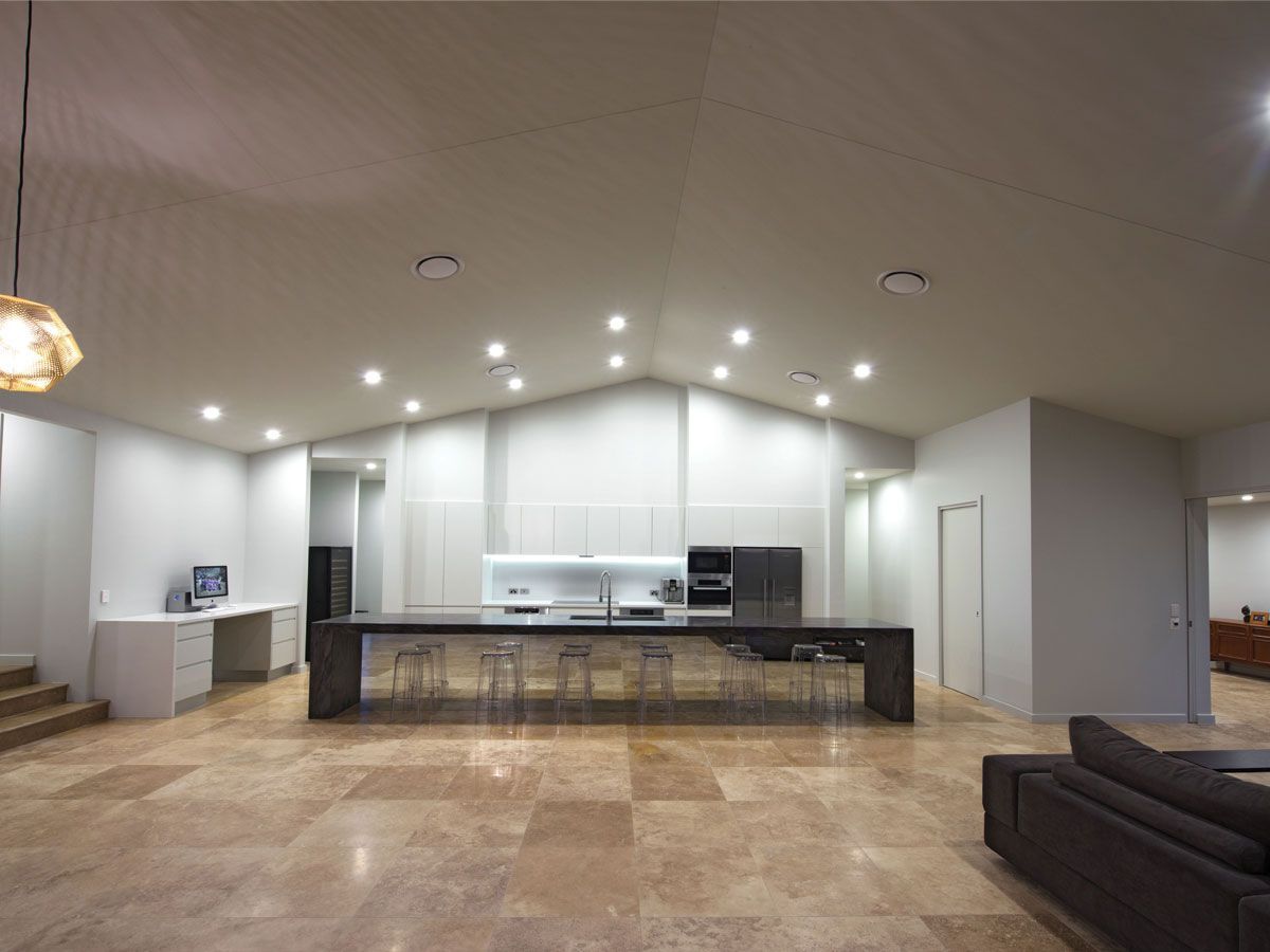 Open-plan kitchen and living room with white cabinets, black island, tile floor, and brown sofa.