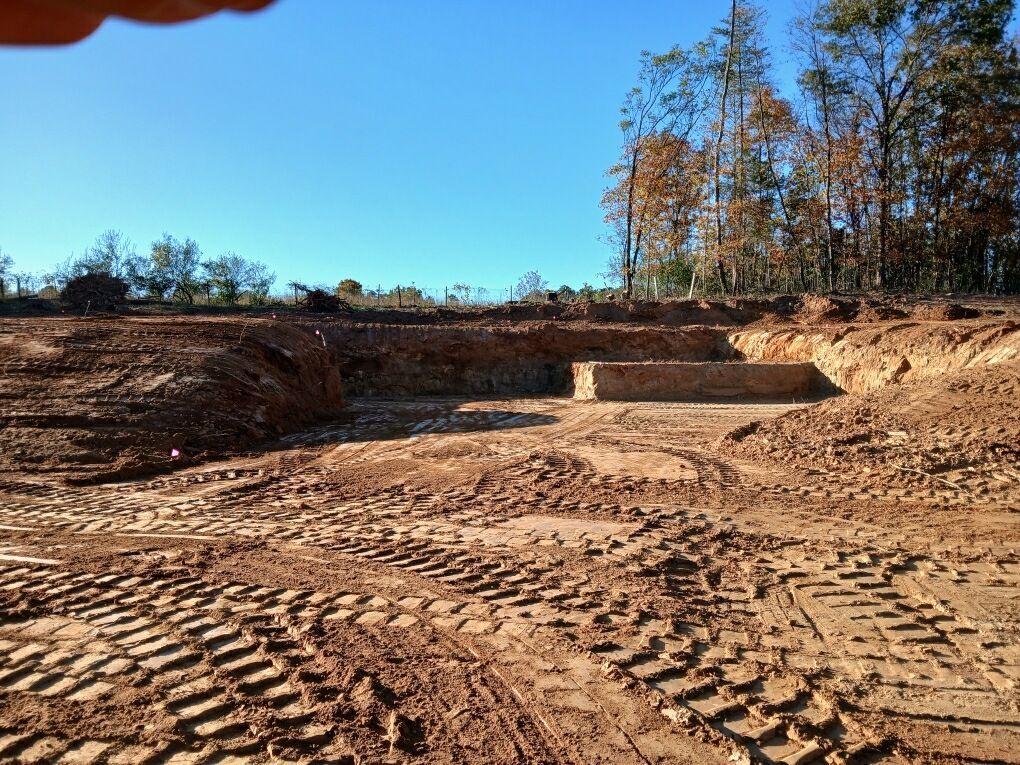 Construction site; excavated earth, tire tracks, and a retaining wall under a blue sky.
