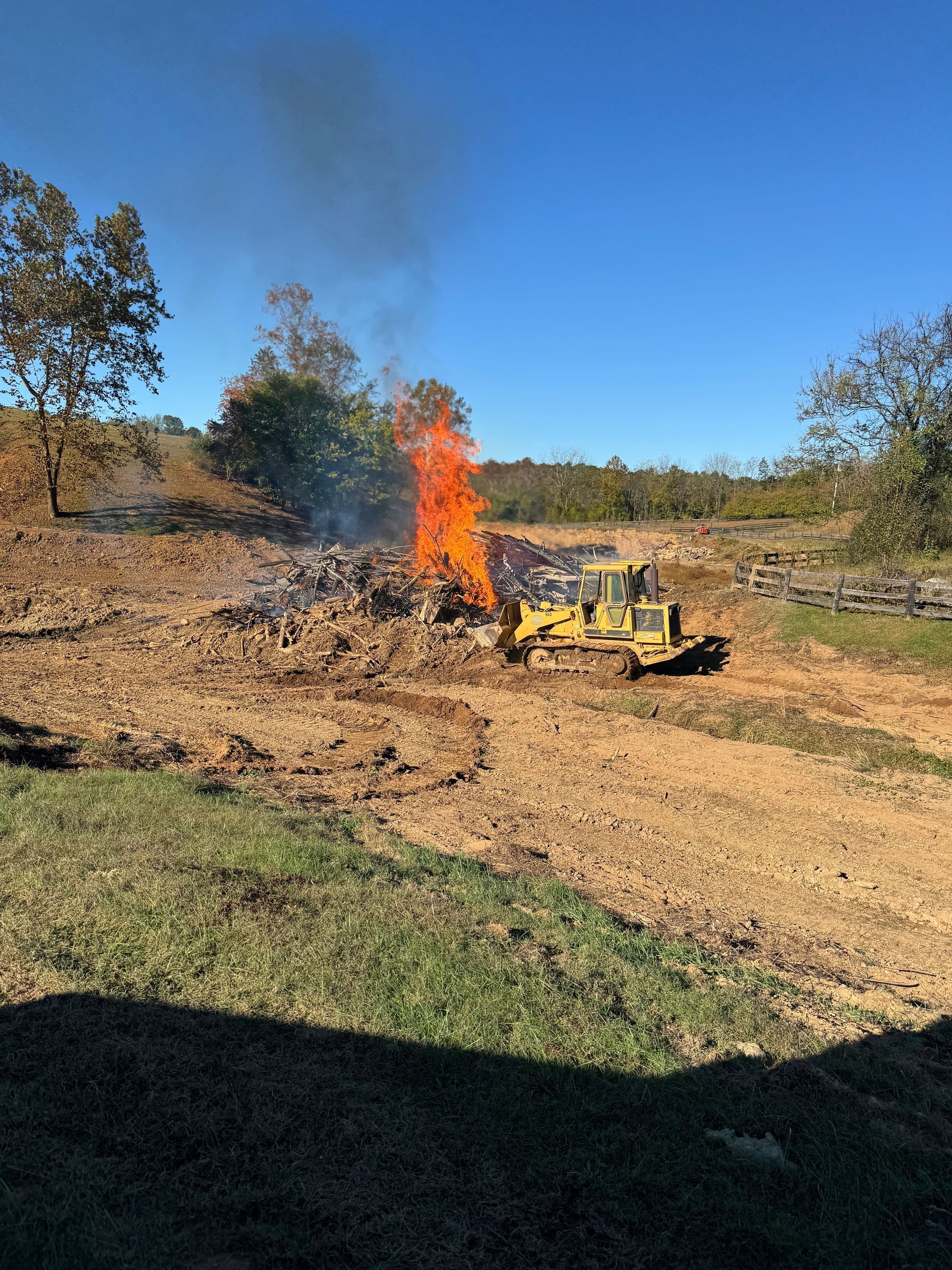 Bulldozer near a large fire in a field on a sunny day.