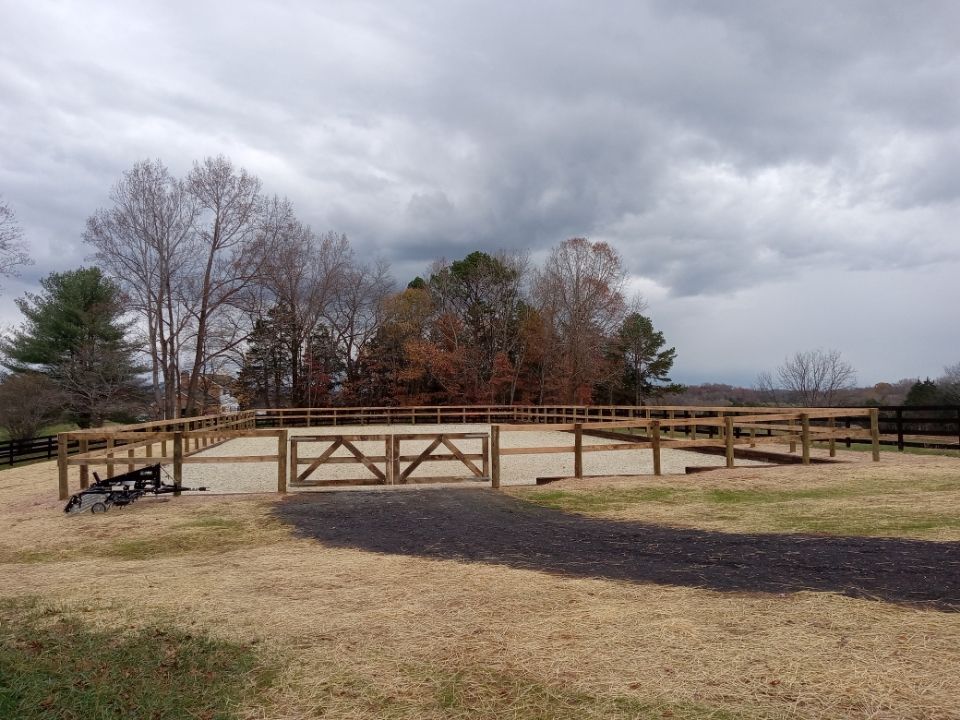 Horse riding arena enclosed by a wooden fence, under an overcast sky.