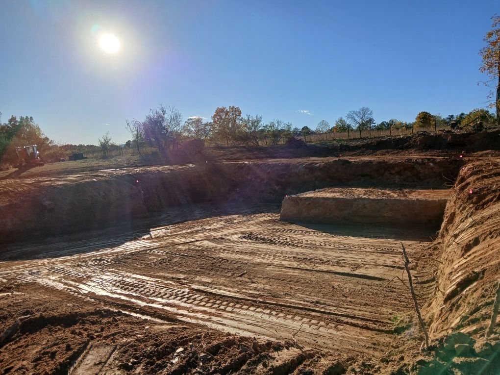 Construction site, muddy earth, tiered levels, bright sun in clear blue sky.