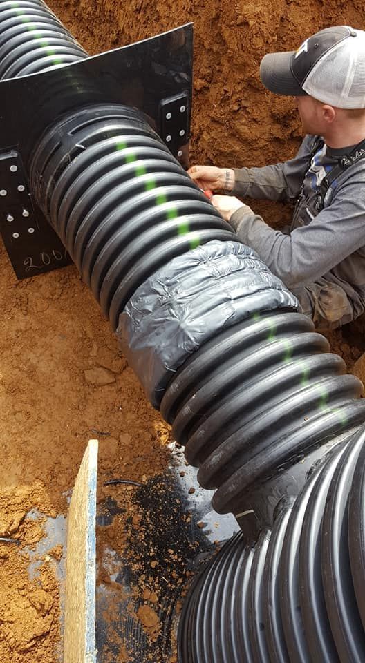 Man working on corrugated drain pipes in a dirt trench, using tape.