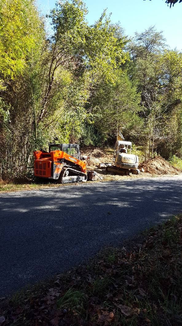 Orange and white construction equipment parked on the side of a road, surrounded by trees.