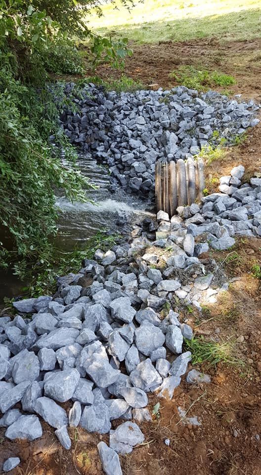 Stream of water flowing through rocks and a corrugated pipe in a grassy bank.