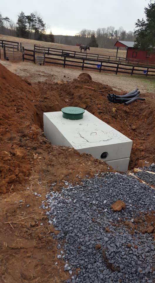 Concrete septic tank installed in a dug trench with gravel and a rural landscape background.