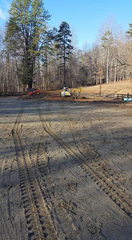 Dirt parking area with tractor tire tracks; trees in background, construction equipment visible.