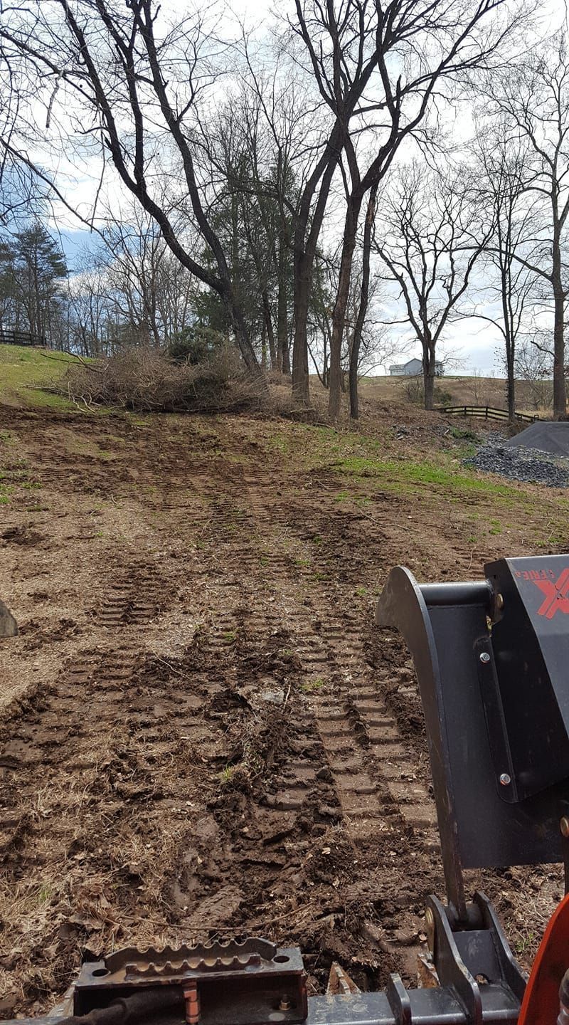 A muddy construction site with tracks, trees in background, bright sky.