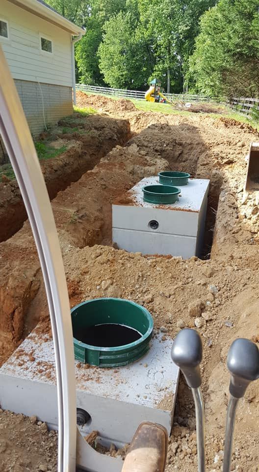 Septic tank installation in progress; concrete tanks in an excavated trench, with green access lids.