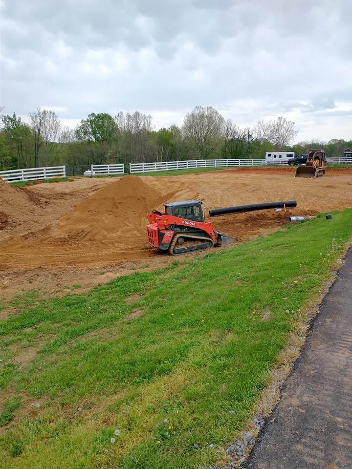Red skid steer on a construction site with dirt and a large pipe, green grass in foreground.