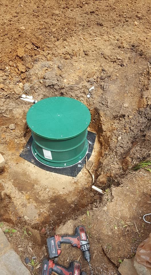 Green septic tank in a dirt pit with tools.