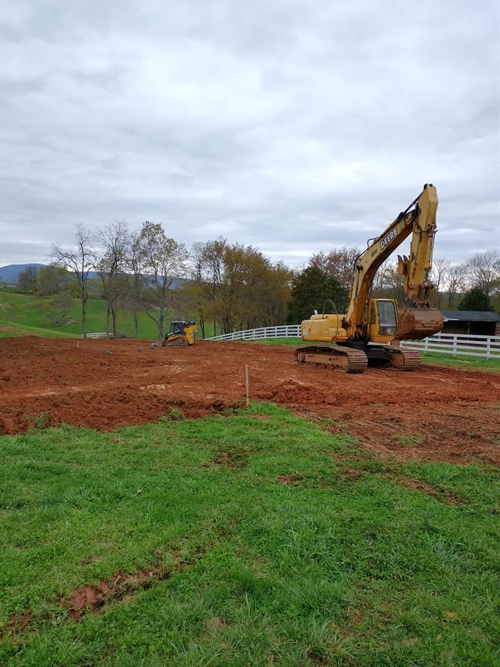Excavator and small dozer on a cleared, red-soil construction site, overcast sky above.