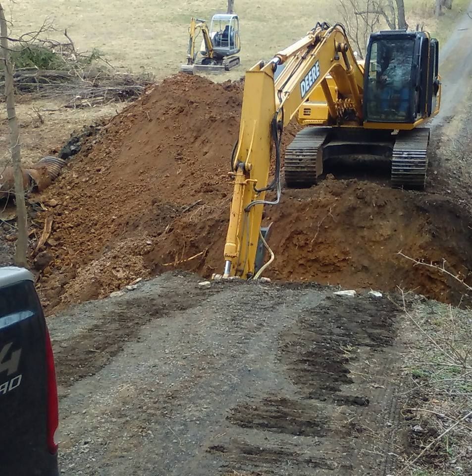 Yellow excavator digging into a dirt pile on a gravel road, with a smaller excavator in the background.