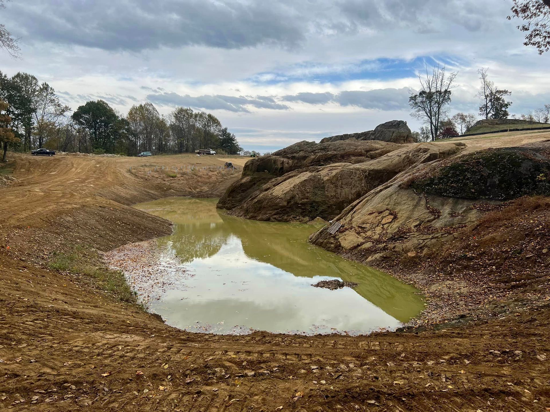 A muddy pond in a dirt landscape under a cloudy sky.