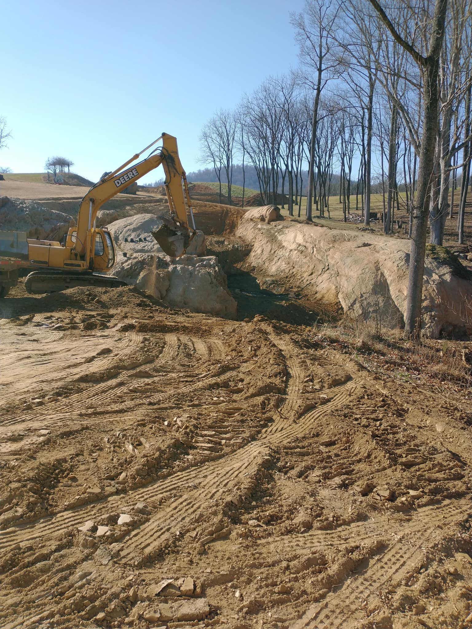 Yellow excavator digging into a dirt embankment, creating a large excavation pit. Sunny day.