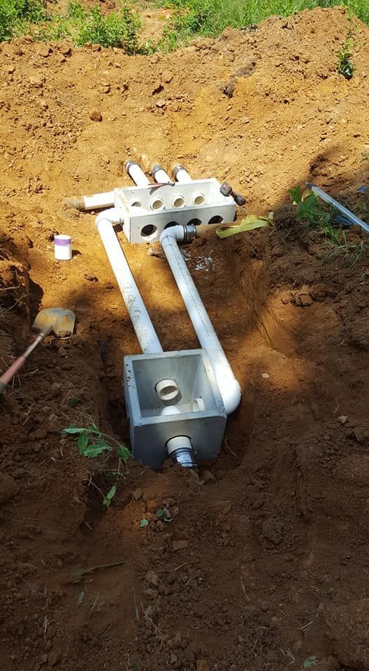 Pipes and boxes buried in dirt. PVC pipes connect two white plastic boxes, in an outdoor setting.