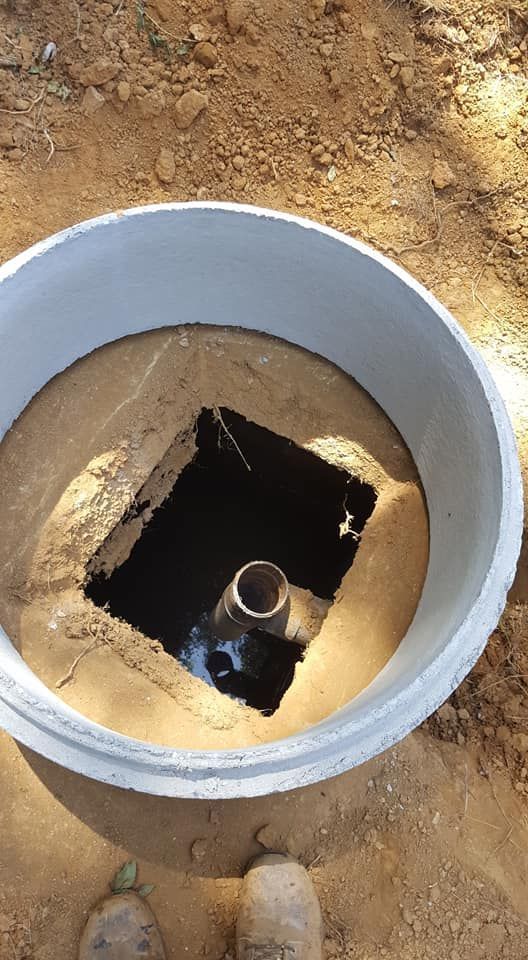 Concrete ring surrounding a square opening. A pipe protrudes from the center of the opening, set in dirt.