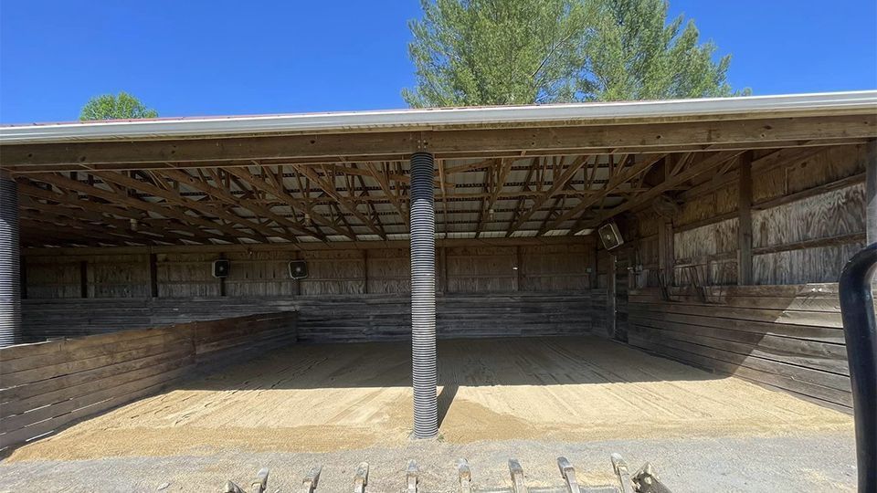 Empty wooden barn with a gravel floor, under a sunny sky.