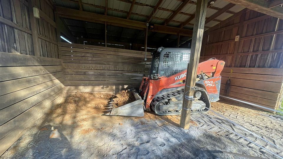 Orange skid steer loader inside a wooden structure, scooping material.