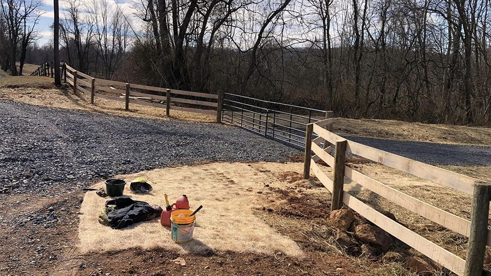 Gravel driveway with wooden fence, tools in foreground, trees in background, sunny day.