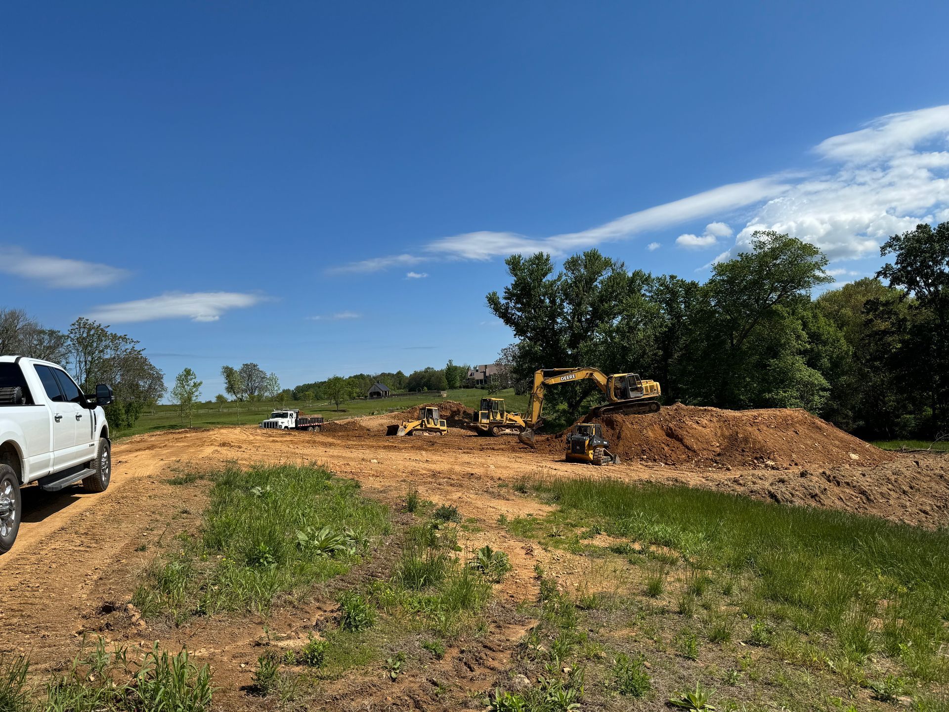Construction site with a white truck, dirt piles, and equipment under a blue sky.