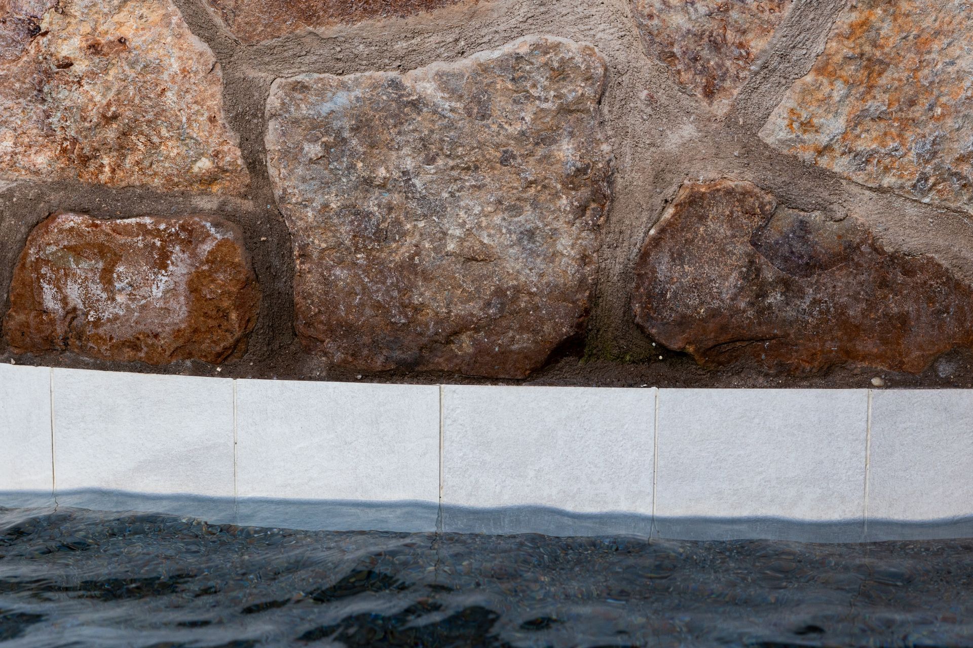 Stone wall above a waterline with white tiles. Water surface visible.