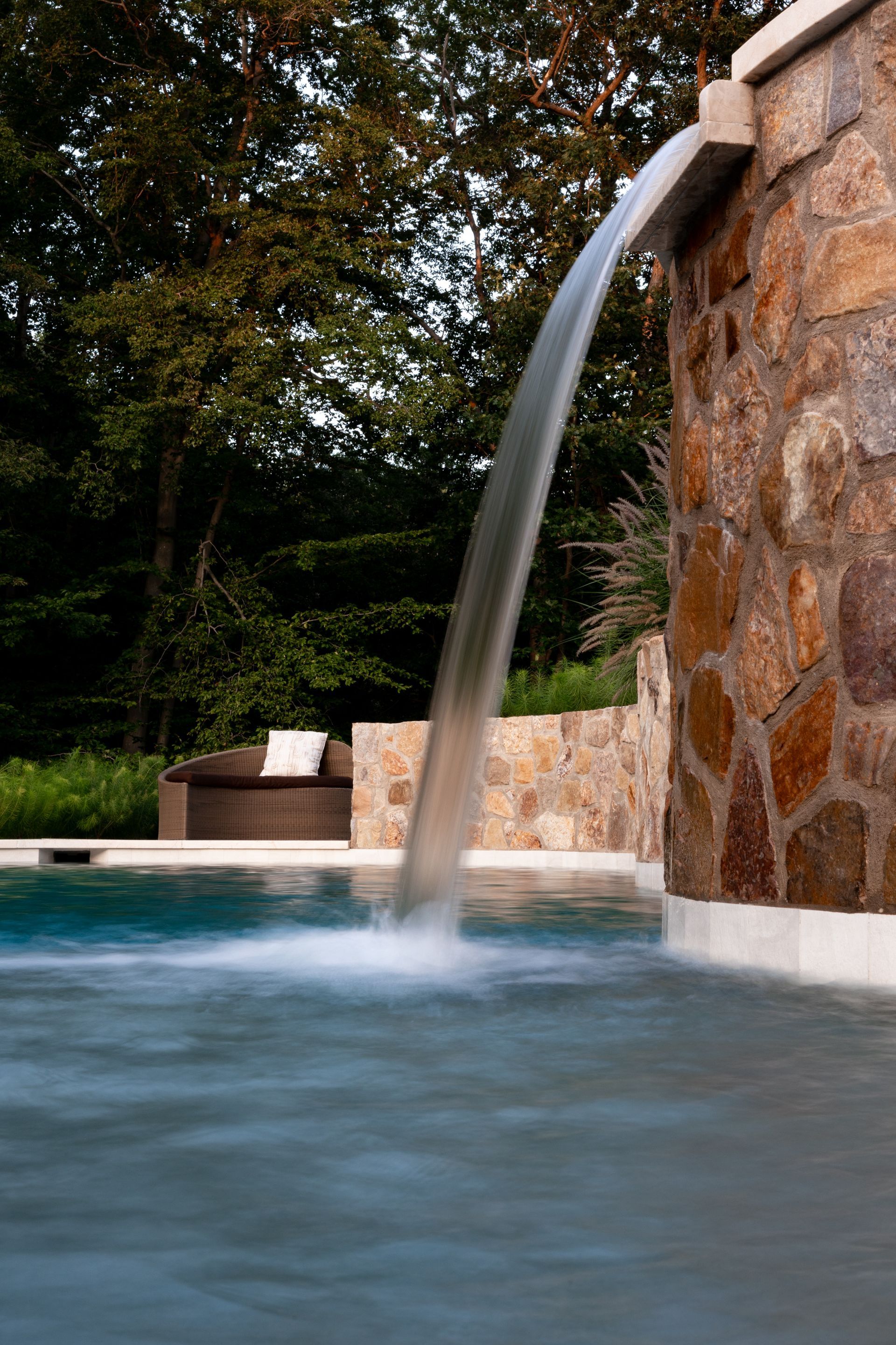 Water cascading from a stone wall into a pool, with trees in the background.