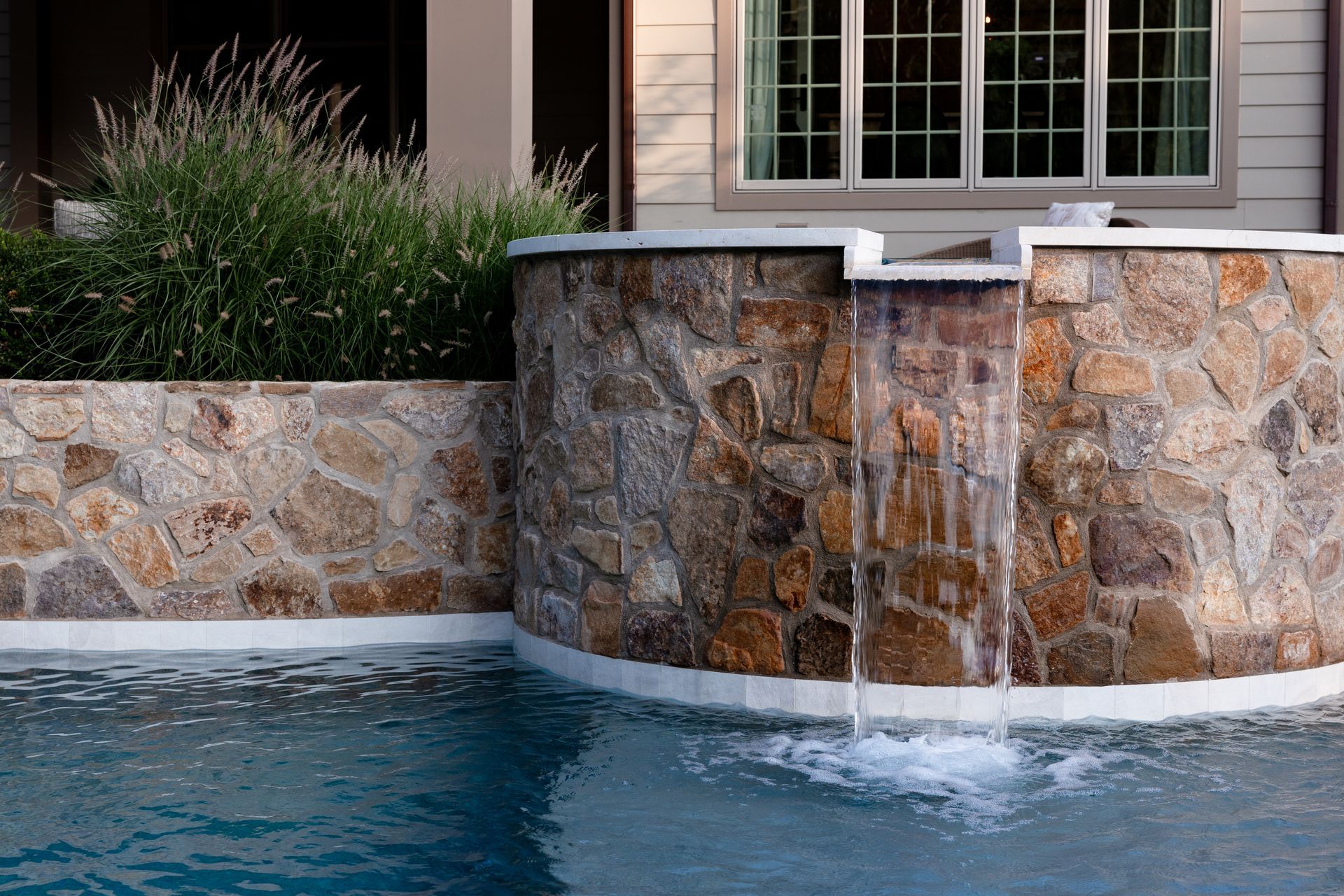 Stone wall with waterfall feature flowing into a swimming pool.