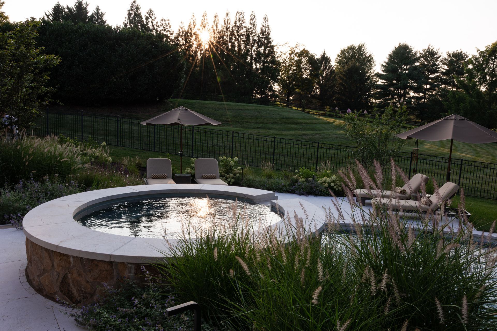 Circular pool and lounge chairs on a patio with a grassy hill in the background. Sunset casts a golden light.