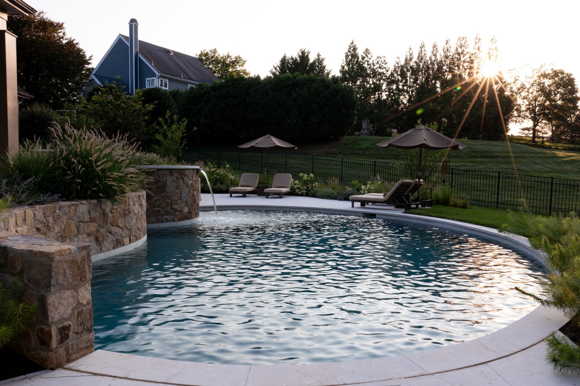 Pool with stone accents, lounge chairs, and umbrella with a sunny background.