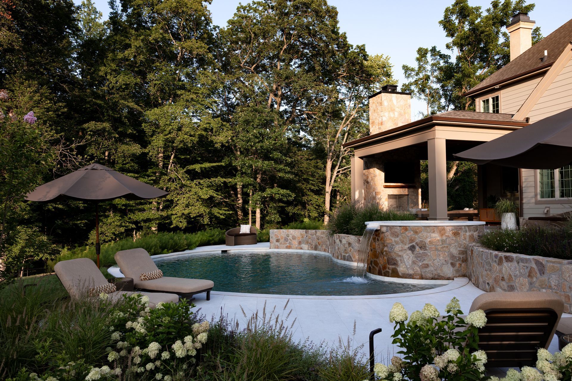 A luxurious backyard with a pool, lounge chairs, and an outdoor kitchen area surrounded by lush greenery.