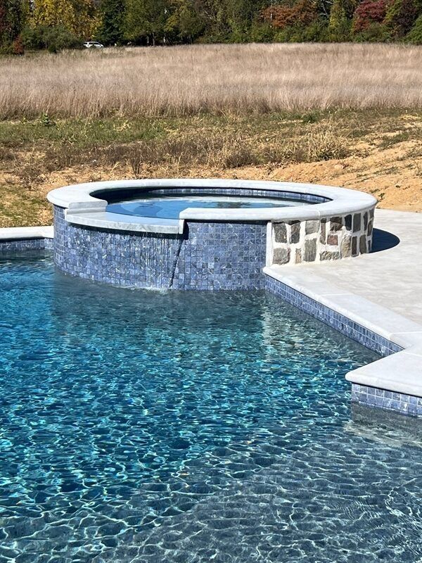 Swimming pool with attached hot tub, blue tile, stone accents, and surrounding concrete deck.