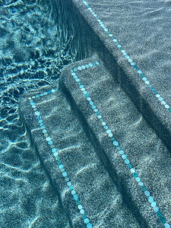 Blue-tiled pool steps with a textured surface, filled with clear water, and a decorative blue tile border.