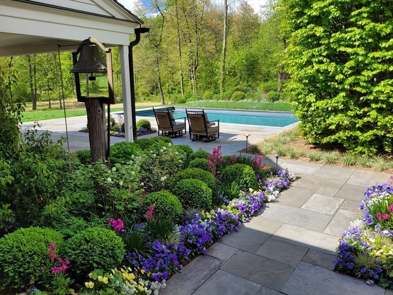 Stone patio with blooming flowers and a swimming pool in a lush garden.