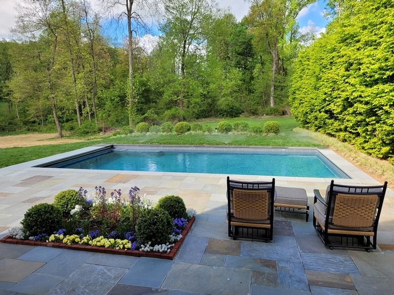 Backyard with pool, stone patio, lounge chairs, and landscaping.