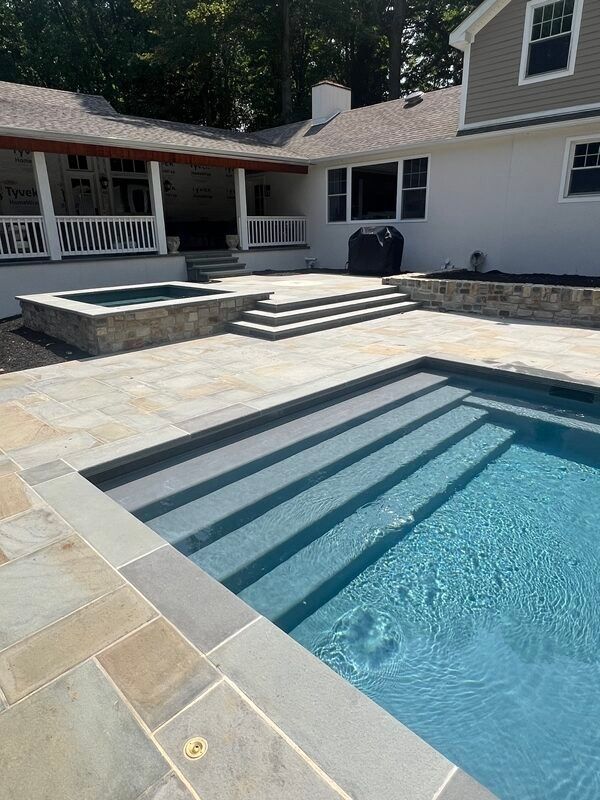 Backyard pool and spa with stone patio and stairs leading to a house.