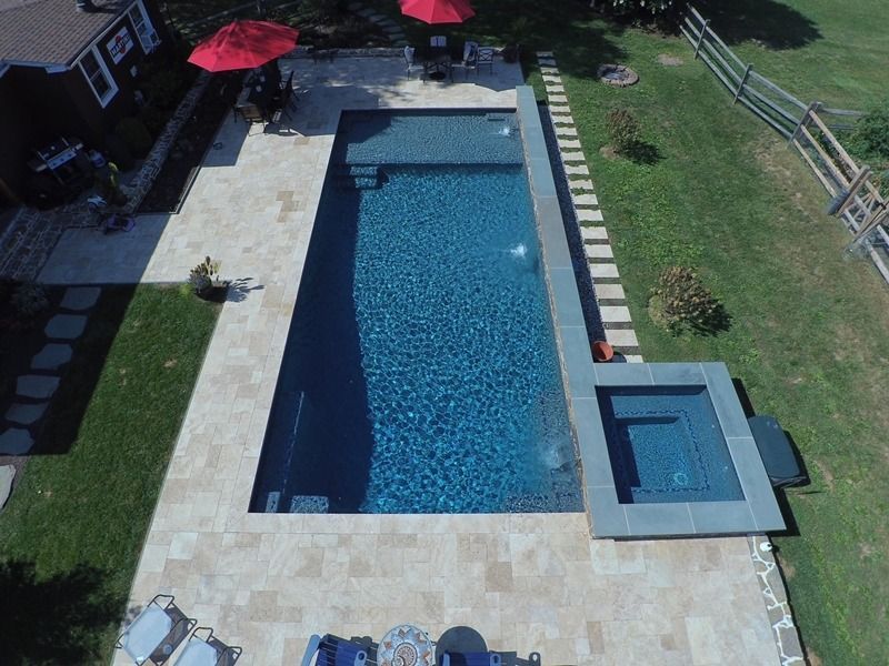 Aerial view of a rectangular pool with a spa. Beige patio surrounds pool; green lawn and red umbrellas visible.