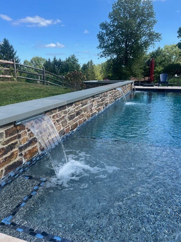 Swimming pool with stone waterfall feature, blue water, sunny day.