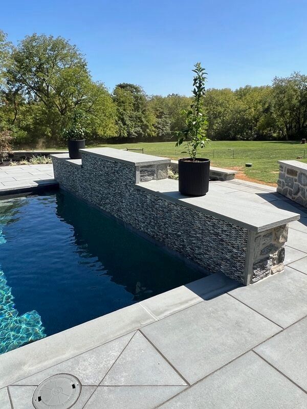 Pool with stone walls, steps, and potted plants on a sunny day.