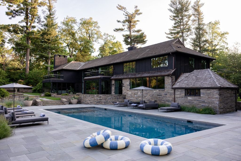 Luxury house with pool. Black exterior, stone facade, blue pool, lounge chairs, and inflatable rings.