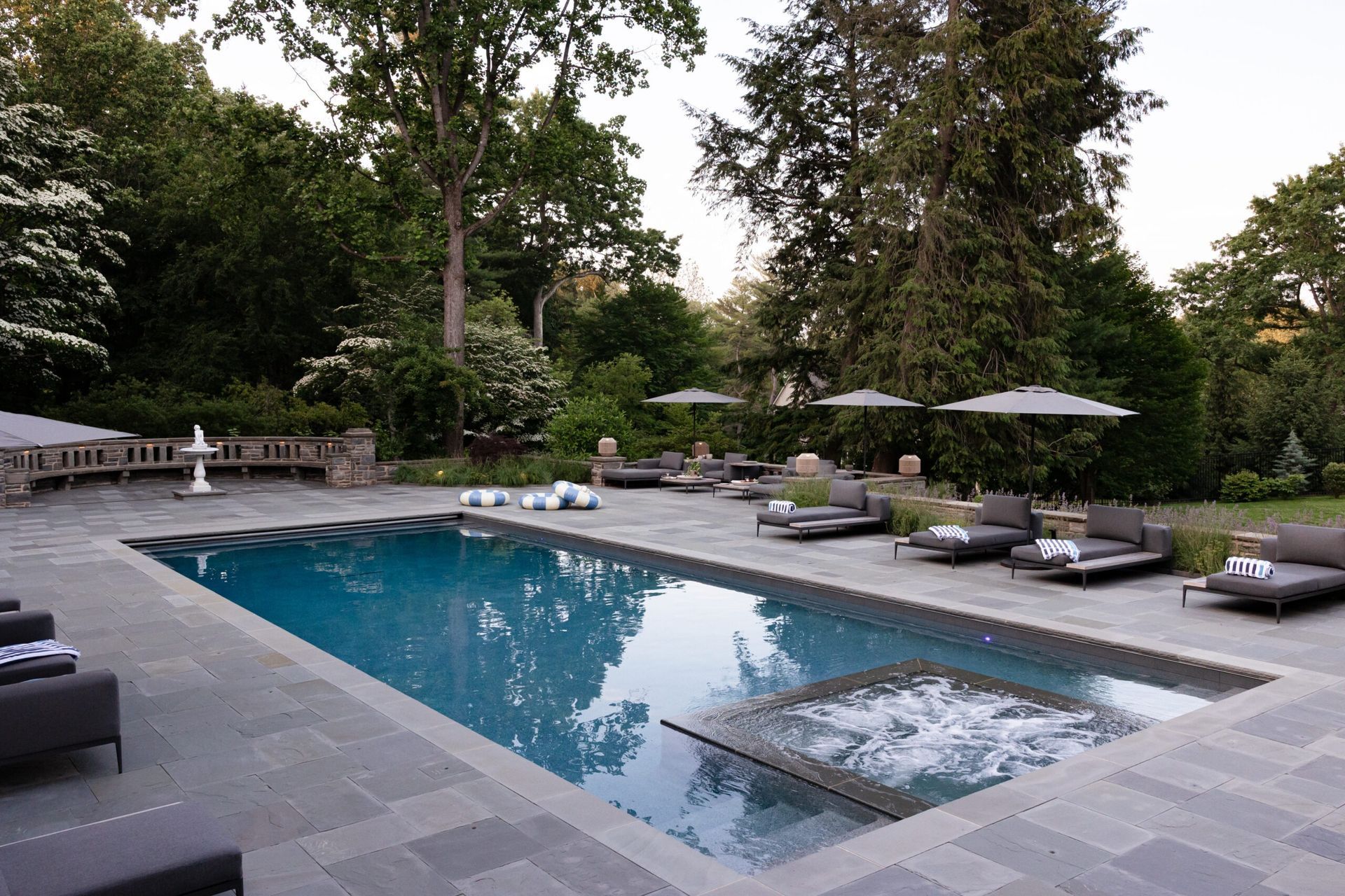 Pool with lounge chairs and umbrellas in a garden setting, surrounded by trees.