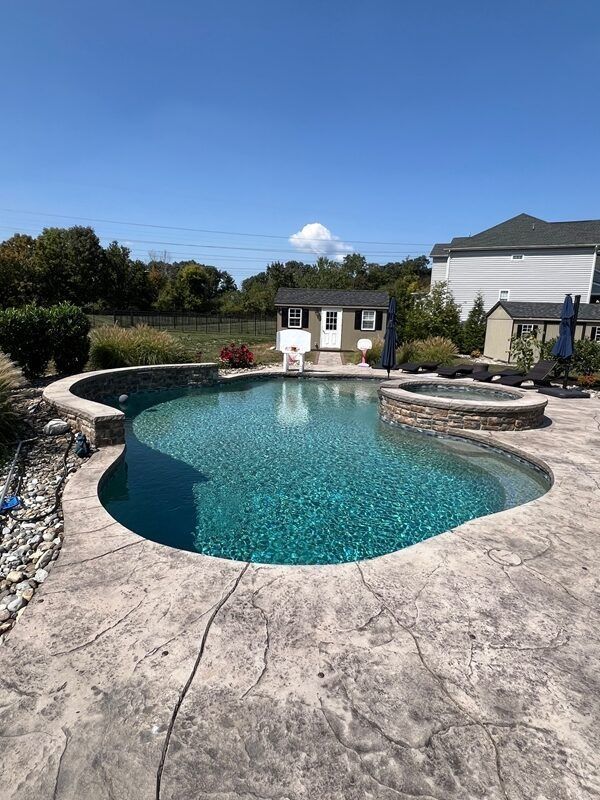 Outdoor swimming pool with stamped concrete patio, blue sky, and small shed.