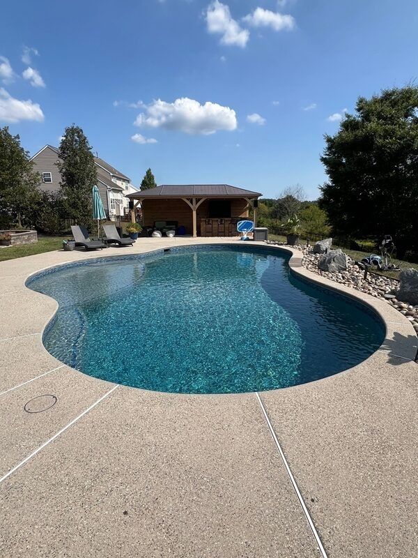 Swimming pool with blue water, concrete deck, and wooden gazebo on a sunny day.