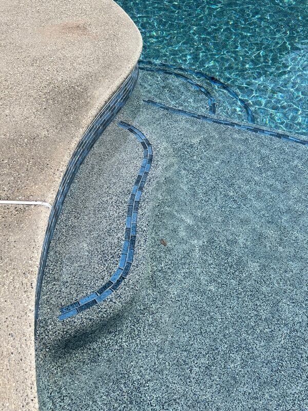 Pool steps with blue tile accent, concrete edge, and turquoise water.