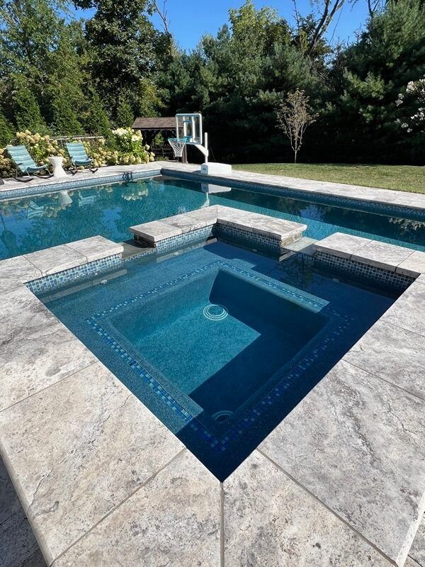 Pool with dark blue tile and a raised hot tub with travertine border.