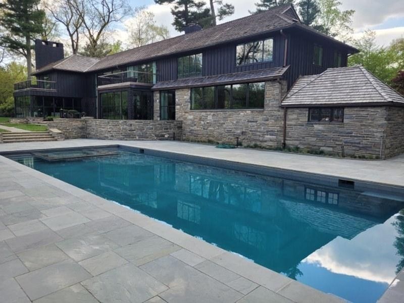 Dark house with a pool. Black exterior, stone accents, and a rectangular pool with blue water.