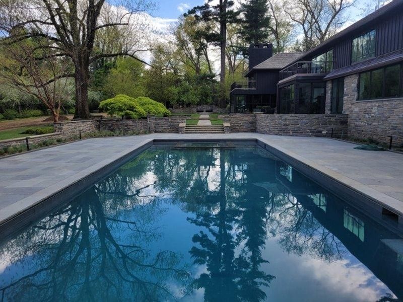 Rectangular pool reflects trees and sky; stone walls frame yard with modern house.