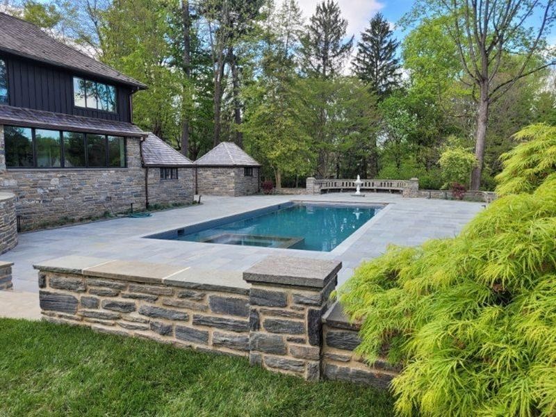 Pool area with stone walls, pool, small stone buildings, green foliage, and trees.