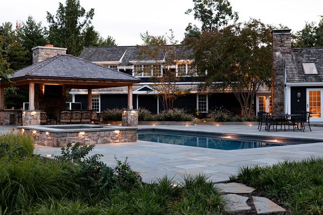 Stone house with a covered patio and swimming pool, surrounded by trees at dusk