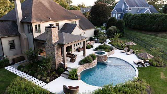 Aerial view of a house with a curved backyard pool, stone patio, and landscaped lawn